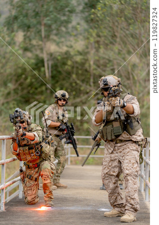 Vertical image military or soldier team with battle suit stay on the bridge near flare firework in position for battle and point gun different direction during outdoor practice. Vertical image military or soldier team with battle suit stay on the bridge near flare firework in position for battle and point gun different direction during outdoor practice. 119827324