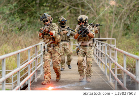 Group of military or soldier team with battle suit walk on the bridge near flare firework and point gun in forward direction during outdoor practice. 119827608