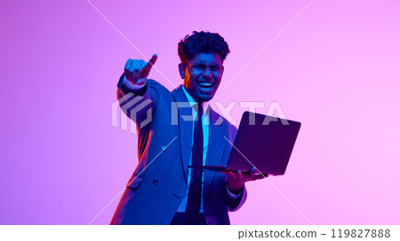 Portrait of happy, excited, smiling Indian man in formal wear holding laptop and gesturing, showing success against purple studio background in neon light Portrait of happy, excited, smiling Indian man in formal wear holding laptop and gesturing, showing success against purple studio background in neon light 119827888