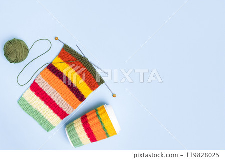 Cup for takeaway coffee with knitted autumn striped cover and knitted wool with knitting needles on blue background. Concept of takeaway coffee, walking, energetic life, hobbies needlework 119828025