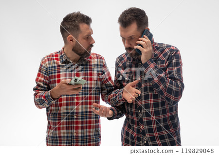 Two identical men in plaid shirts, one on call, other holding phone, intensely engaged, appearing to clarify or debate against white studio background. 119829048