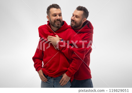 Two young stylish dressed men, twins standing together and hugs, expressing love and support against white studio background. 119829051