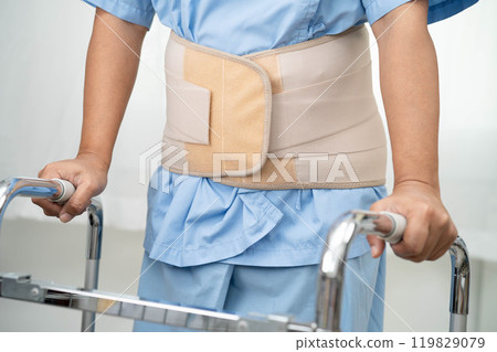Asian senior pain back wearing elastic support belt with walker. 119829079