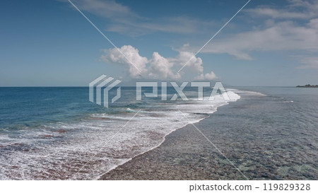 Turquoise blue water gently rolling shallow rocky shoreline. The deep blue sky is dotted with fluffy white clouds. Tropical island shore, serene idyllic paradise. Natural beauty landscape background 119829328