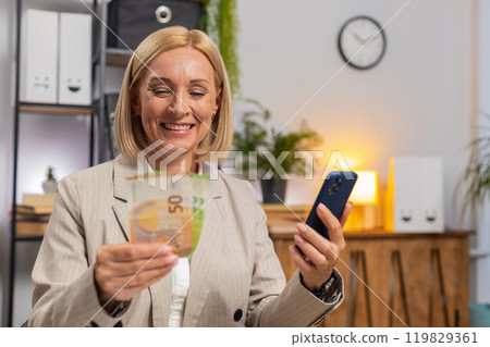 Mature businesswoman counting money euro cash using smartphone calculator app at home office desk 119829361