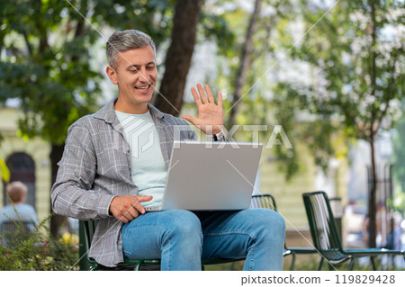 Mature man sitting in city street looking at laptop camera making video webcam conference call 119829428