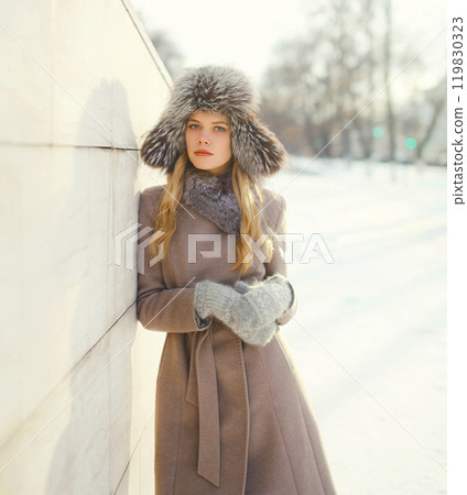 Beautiful woman wearing a coat jacket and hat over snow in winter city 119830323