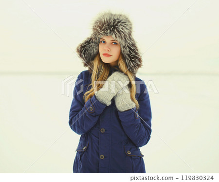 Beautiful woman wearing a coat jacket and hat over snow in winter day 119830324