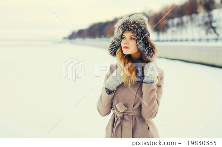 Fashion winter portrait beautiful young woman wearing a coat jacket and hat over snow 119830335