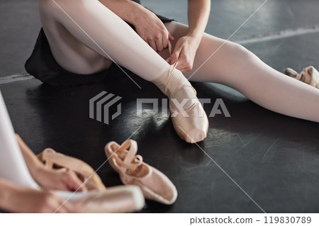 Cropped shot of teenage girl tying up satin ballet shoes with ribbons preparing for class while sitting on floor in dance studio, copy space 119830789