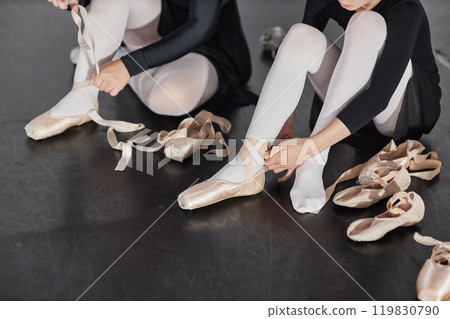 Cropped shot of young girl tying up satin ballet shoes with ribbons preparing for dance class while sitting on floor in studio, copy space 119830790