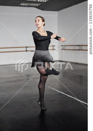 Full length shot of confident female ballet dancer dressed in leotard and skirt for dancing performing pirouettes with ease and grace, during exercise daily routine in dance studio 119830798