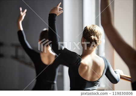 Medium shot of young female dance teacher in black leotard gracefully moving arms practicing ballet positions while teaching little kids in studio, copy space Medium shot of young female dance teacher in black leotard gracefully moving arms practicing ballet positions while teaching little kids in studio, copy space 119830806