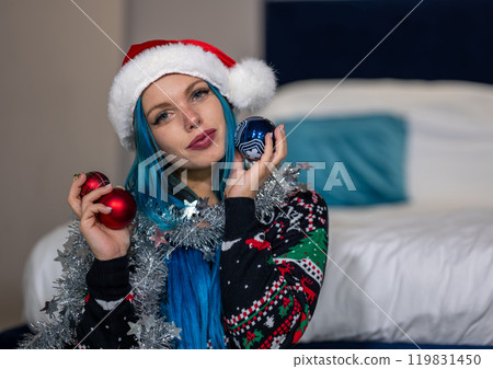 Portrait of a beautiful hipster Caucasian woman in Christmas clothes.She poses looking at the camera holding colorful balls and a silver decoration around her neck.Beauty,Christmas holidays,positivity 119831450