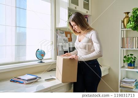 Young woman at home unpacks cardboard box with online purchases Young woman at home unpacks cardboard box with online purchases 119831713