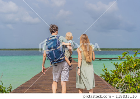 Mom, dad and their baby son exploring wooden pier over the turquoise waters of Bacalar Lake, Mexico. Peaceful tropical travel destination concept Mom, dad and their baby son exploring wooden pier over the turquoise waters of Bacalar Lake, Mexico. Peaceful tropical travel destination concept 119833110