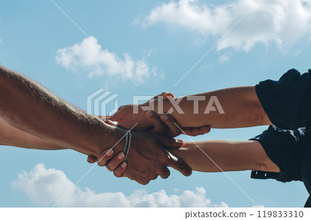Two hands holding each other firmly against a bright sky, symbolizing support and connection. 119833310