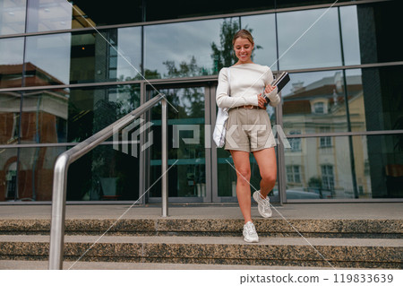 A Young Woman Walking Gracefully Down the Stairs, Dressed in a Chic and Trendy Outfit A Young Woman Walking Gracefully Down the Stairs, Dressed in a Chic and Trendy Outfit 119833639