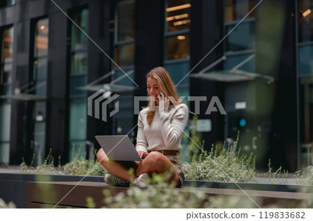A Young Woman is Working on Her Laptop in a Vibrant Urban Setting Surrounded by City Life 119833682