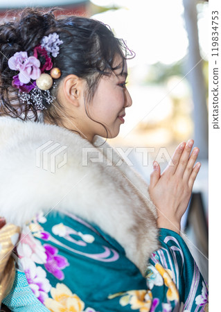 A young woman in formal attire praying at a shrine 119834753