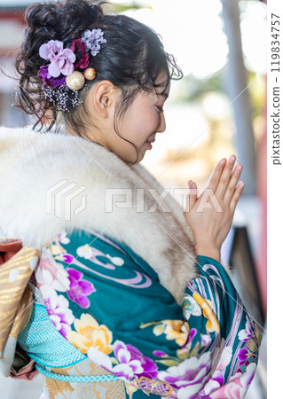 A young woman in formal attire praying at a shrine 119834757