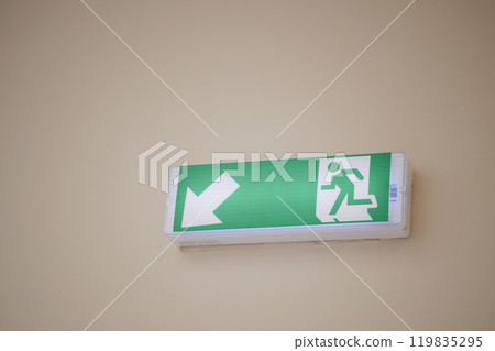An Illuminated Emergency Exit Sign featuring a Left Arrow positioned in a Hallway setting An Illuminated Emergency Exit Sign featuring a Left Arrow positioned in a Hallway setting 119835295