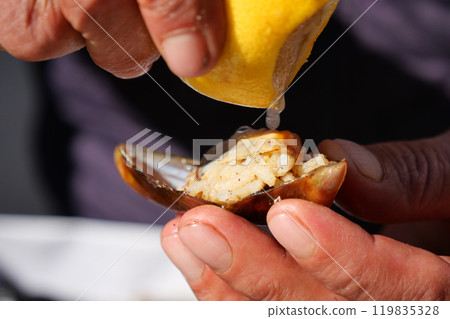 A hand squeezing fresh lemon juice onto a clam shell to enhance the culinary experience, A hand squeezing fresh lemon juice onto a clam shell to enhance the culinary experience, 119835328