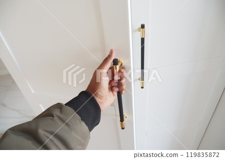 Hand Opening a Stylish and Modern Cabinet Door That Features Beautiful Gold Accents 119835872