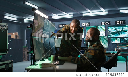 Military officers look at intel folder files on enemy battle formation, comparing with radar images. Army specialists looking at mission case file and equipment screens, camera B 119837511