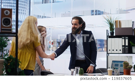 Welcoming financial advisor meeting with clients to recommend financial products and investments, greeting them. Investment strategies expert in workspace doing handshake with customers, camera B 119837605