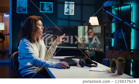 Woman doing software debugging helped by coworker in videocall, checking errors in lines of code. Programmer working from home fixing coding mistakes, assisted by colleague in teleconference, camera B 119837624