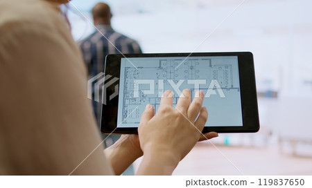 Real estate agent and client evaluating blueprints and discussing the architectural layout of new office space during office tour. Businessman strategizing corporate office relocation deal. Camera A. 119837650