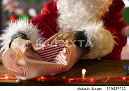 Saint Nicholas decorates a festive present box in his North Pole workshop, preparing wrapped gifts for delivery to children on Christmas eve. Colorful ornaments fill the holiday with magic. Close up. Saint Nicholas decorates a festive present box in his North Pole workshop, preparing wrapped gifts for delivery to children on Christmas eve. Colorful ornaments fill the holiday with magic. Close up. 119837682
