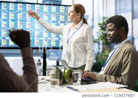 General manager making a presentation with infographics and sales numbers on interactive board, showing the organizational progress to the staff. Employees reviewing analytics plans. General manager making a presentation with infographics and sales numbers on interactive board, showing the organizational progress to the staff. Employees reviewing analytics plans. 119837687