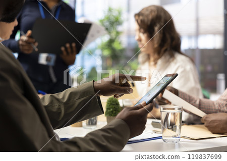 Important business investor studying development progress reports on tablet, examining big data visualization tools during a briefing meeting with executive board members. Management. 119837699
