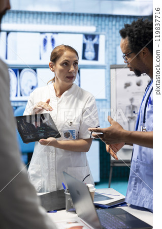 Diverse doctors team looking at radiography scan test result to check organs condition, examining liver and lungs to fight illness. Group of physicians discussing healthcare services for wellness. Diverse doctors team looking at radiography scan test result to check organs condition, examining liver and lungs to fight illness. Group of physicians discussing healthcare services for wellness. 119837716