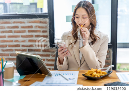 Young businesswoman eating unhealthy snack, french fried, while working on her project at her desk 119838600
