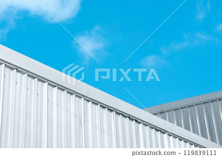 Industrial warehouse factory buildings with silver corrugated steel wall against blue sky background, low angle view. 119839111