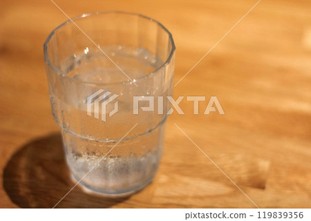 A cold glass of water filled with ice and its shadow on the table A cold glass of water filled with ice and its shadow on the table 119839356
