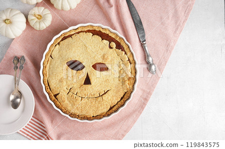 Halloween food. Homemade pumpkin pie or tart with a scary face for Halloween on a red napkin on gray table. Copy space. Halloween food concept. top view Halloween food. Homemade pumpkin pie or tart with a scary face for Halloween on a red napkin on gray table. Copy space. Halloween food concept. top view 119843575