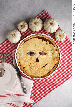 Halloween food. Homemade pumpkin pie or tart with a scary face for Halloween on a red napkin on gray table. Copy space. Halloween food concept. top view 119843577