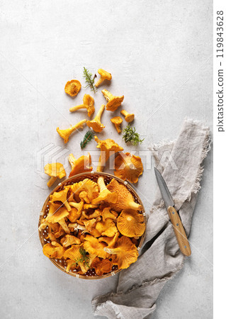 Top view of a bowl full of chanterelle mushrooms (Cantharellus cibarius). The bowl is on a gray background with a few more mushrooms. 119843628
