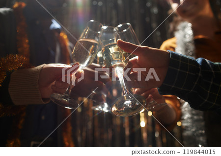 Cropped shot of people clinking glasses of champagne standing in top light while celebrating Christmas with silver tinsel in background at home party, copy space Cropped shot of people clinking glasses of champagne standing in top light while celebrating Christmas with silver tinsel in background at home party, copy space 119844015