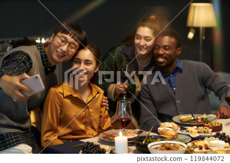 Candid shot of Asian man taking selfie with four cheerful friends while sitting at festive dining table celebrating Christmas at home party, copy space Candid shot of Asian man taking selfie with four cheerful friends while sitting at festive dining table celebrating Christmas at home party, copy space 119844072