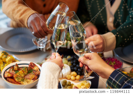 Cropped shot of people raising toast clinking glasses with champagne at friends gathering while celebrating Christmas together at home dinner, copy space Cropped shot of people raising toast clinking glasses with champagne at friends gathering while celebrating Christmas together at home dinner, copy space 119844111