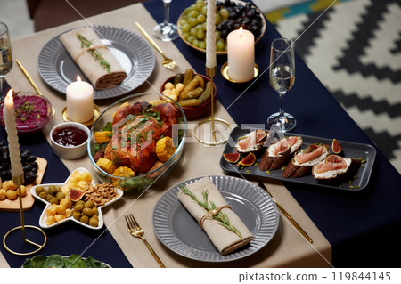 High angle shot of dinner plate with linen napkin decorated with branch of rosemary served on festive table with roasted chicken and candles lit on Christmas Eve, copy space High angle shot of dinner plate with linen napkin decorated with branch of rosemary served on festive table with roasted chicken and candles lit on Christmas Eve, copy space 119844145