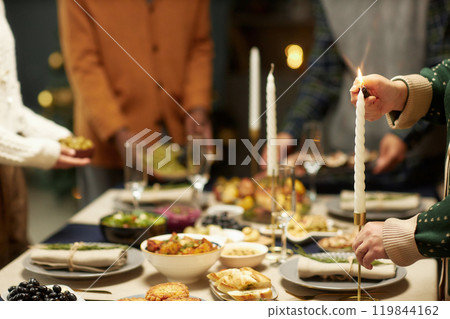 Cropped shot of woman lighting candlestick while serving festive dinner together with family on Christmas Eve, copy space 119844162