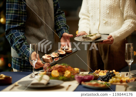 Cropped shot of man serving plate of tartines with figs and ricotta on dining table and woman helping while preparing for family Christmas dinner Cropped shot of man serving plate of tartines with figs and ricotta on dining table and woman helping while preparing for family Christmas dinner 119844176