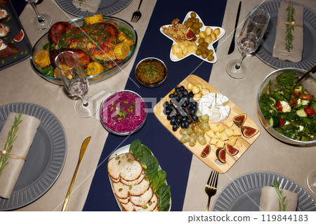 High angle shot of cheese and fruit platter on wooden board and roasted chicken served on festive table setting on Christmas Eve, camera flash, copy space High angle shot of cheese and fruit platter on wooden board and roasted chicken served on festive table setting on Christmas Eve, camera flash, copy space 119844183
