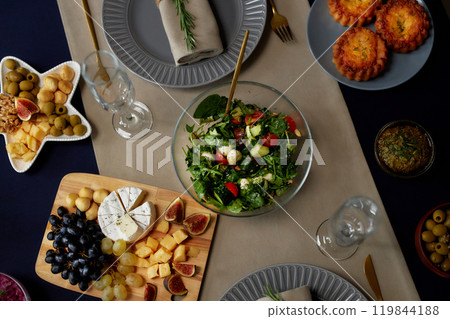Top view of glass bowl with fresh salad and cheese platter served as appetizer at festive dining table for Christmas dinner, copy space 119844188